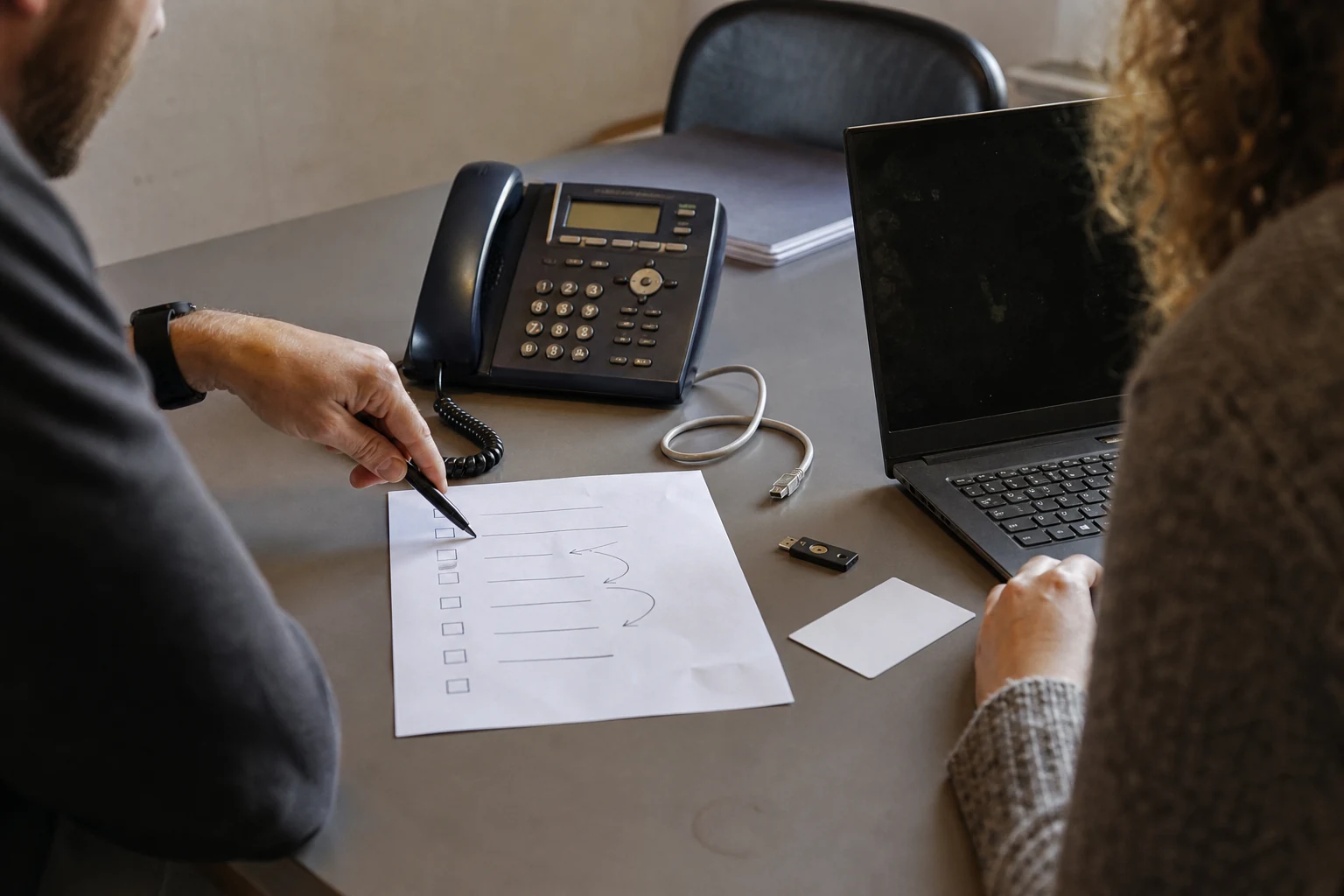 IT und Einkauf prüfen Telefon, Hardware-Schlüssel und Anbieterunterlagen an einem Besprechungstisch